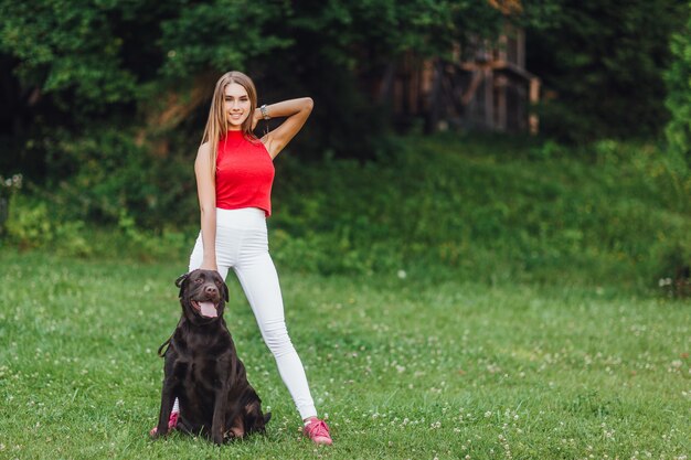 Muchacha hermosa joven con su perro negro Labrador en el parque.