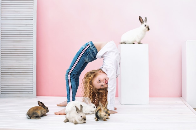 Muchacha hermosa del niño con el pelo rizado y con los animales esponjosos conejos sobre fondo rosa