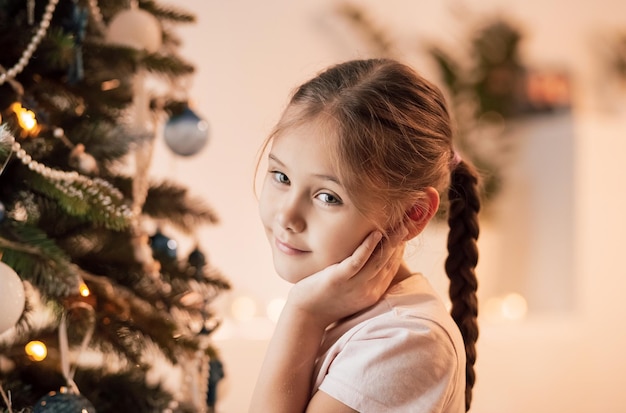 Muchacha hermosa del niño que se coloca cerca de un árbol de Navidad. Concepto de navidad.