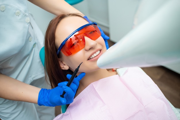 La muchacha hermosa con el pelo rojo se está sentando en la silla dental.