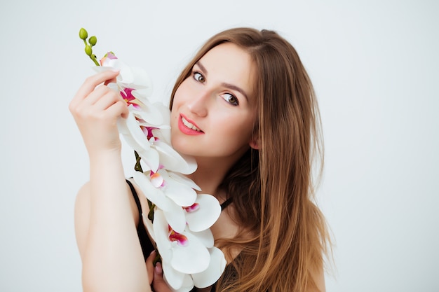 Muchacha hermosa que sostiene una orquídea púrpura delante de su cara.