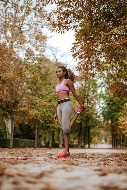 Foto muchacha hermosa de la raza mixta que hace ejercicio al aire libre, en el parque del otoño.