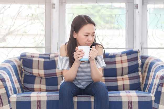 Foto muchacha hermosa en el sofá con la taza del café con leche a disposición.