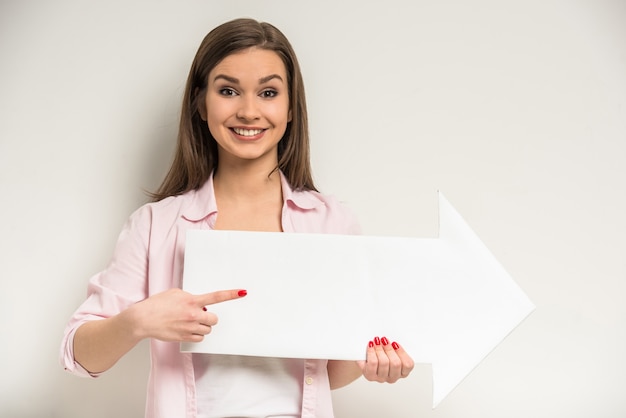 La muchacha hermosa sonriente de los jóvenes está sosteniendo el papel vacío.