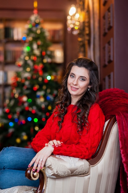 Muchacha hermosa en un suéter rojo cerca del árbol de navidad.