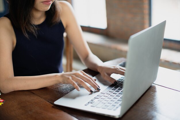 Muchacha independiente asiática que trabaja en la cafetería con una computadora portátil.