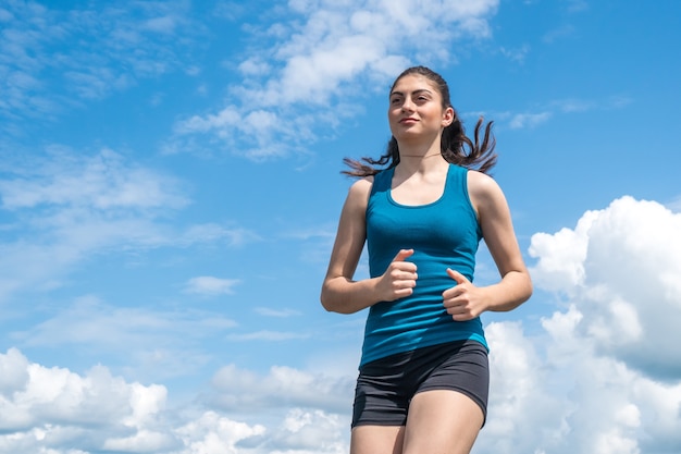 La muchacha joven de los deportes se ejecuta en el cielo azul.