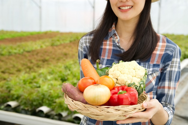 Muchacha joven del granjero que se sostiene diverso de verduras en cesta con sonrisa