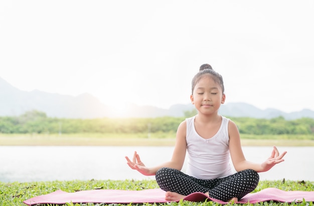 La muchacha linda feliz practica yoga y medita en la posición de loto en parque al aire libre, ejercicio y hea