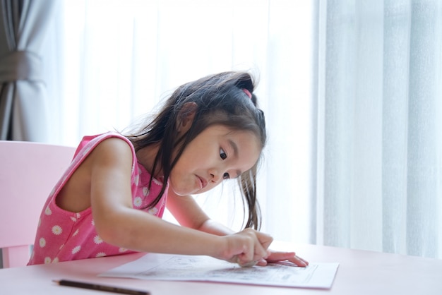 Muchacha linda del niño asiático que usa el borrador en el papel para borrar lo que ella había escrito.