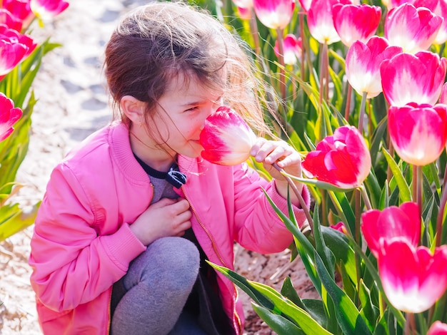 Muchacha linda del niño con el pelo largo que huele la flor del tulipán en campos del tulipán