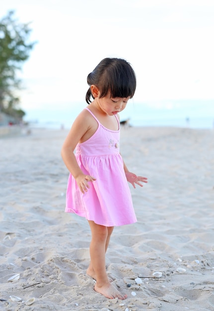 Muchacha linda del niño que se coloca en la playa de la arena