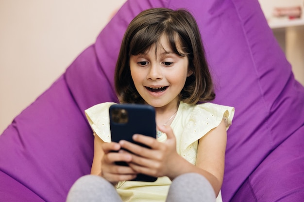 La muchacha linda del niño sostiene al niño del teléfono usando el niño del teléfono inteligente navegando por internet