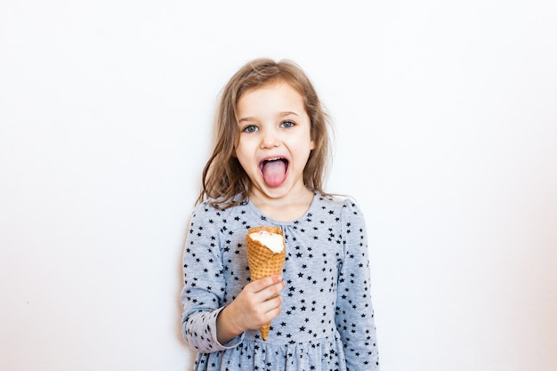 Muchacha linda que come el helado que presenta sobre la pared blanca. ¡Hora de verano!