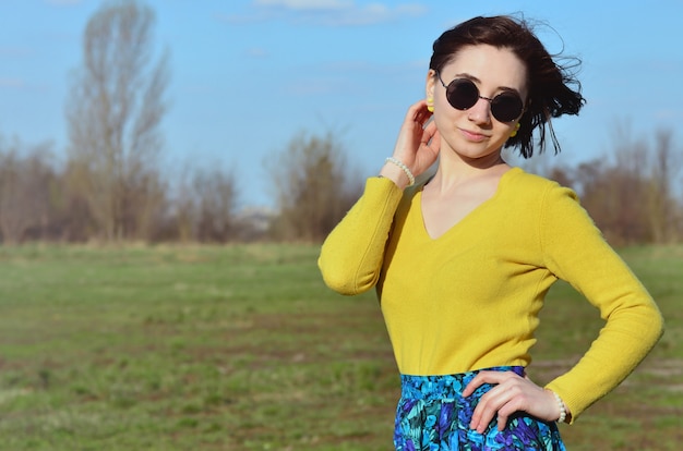 La muchacha morena atractiva y linda en un suéter amarillo camina thro
