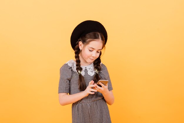 La muchacha muy sonriente sostiene el teléfono inteligente. Niño lindo sobre fondo amarillo, concepto de niños modernos.