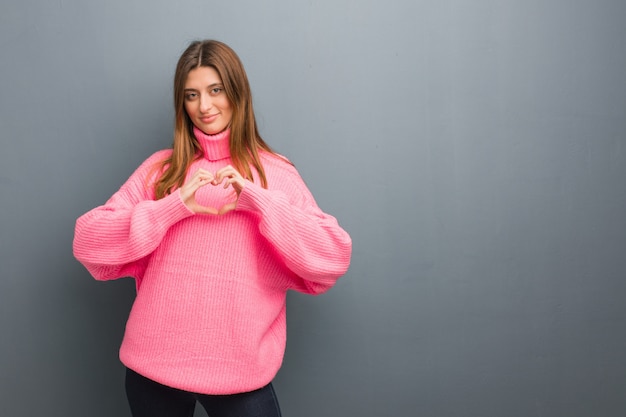 Muchacha natural rusa joven que hace una forma del corazón con las manos