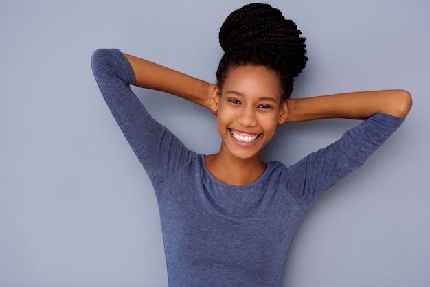 Muchacha negra joven alegre con las manos detrás de la cabeza que sonríe en fondo gris