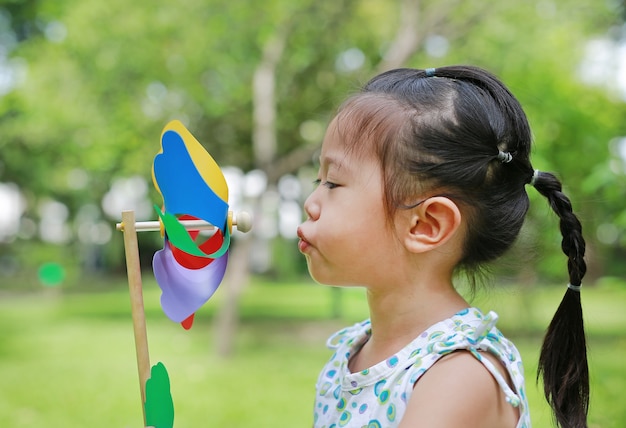 Muchacha del niño pequeño que sopla la turbina de viento en el jardín