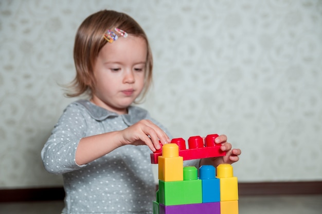 Muchacha del niño que se divierte y construcción de bloques de construcción de plástico brillante. Niño jugando en el piso. Desarrollando juguetes. Aprendizaje temprano.