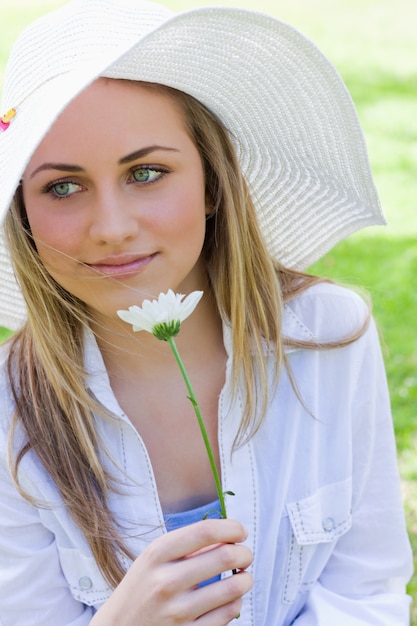 Muchacha pacífica joven que sostiene una flor blanca en un parque