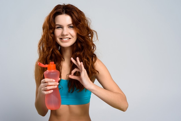 Muchacha pelirroja joven con la botella rosada. Ok Sign.