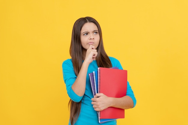 Muchacha pensativa del niño sostenga el bloc de notas para la tarea, la escuela.