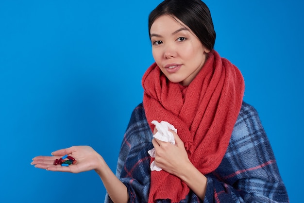 Muchacha con las píldoras que toman frías aisladas en fondo azul.