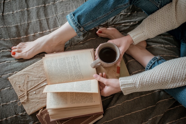 Muchacha que lee un libro y que bebe el café en pies de la cama en la pared.