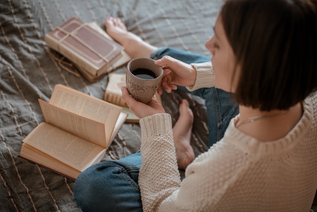 Foto muchacha que lee un libro y que bebe el café en pies de la cama en la pared.