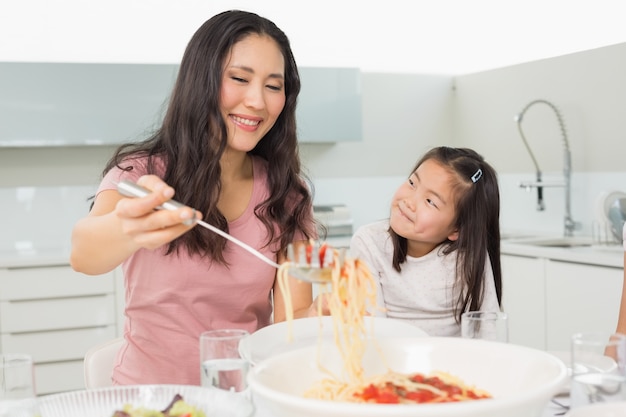 Muchacha que mira a la mujer feliz sirve los espaguetis en cocina