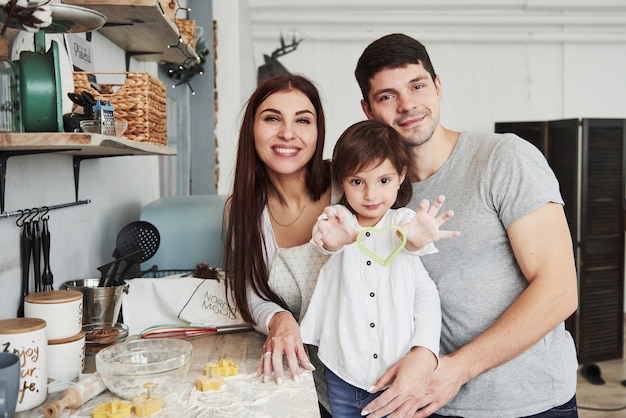 Muchacha que muestra la forma de cocinar en forma de corazón. Cerca de la mesa de la cocina. Linda familia posando para la foto