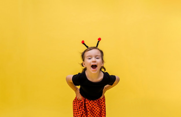 muchacha que ríe en un traje de mariquita en un amarillo aislado