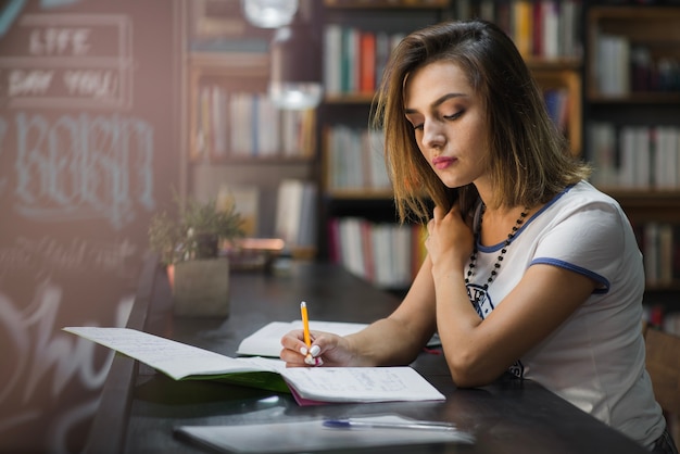 Muchacha que se sienta en la mesa con los cuadernos que escriben