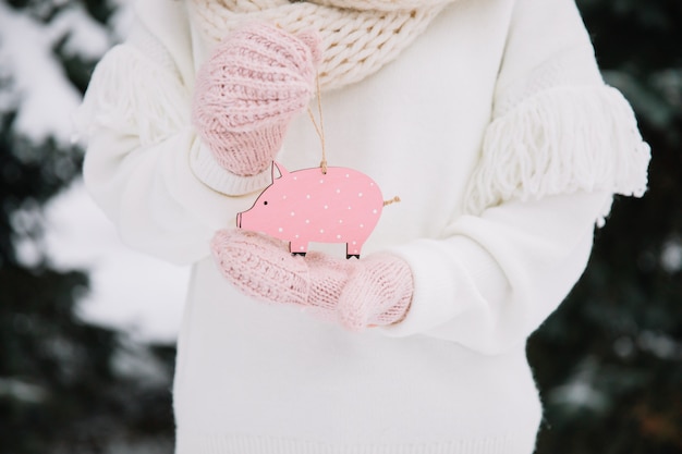 Muchacha que sostiene el cerdo del juguete afuera en el invierno día nevoso frío