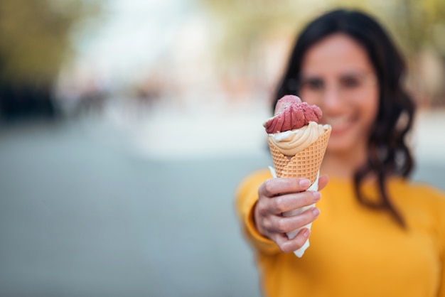 Muchacha que sostiene el cono de helado hacia la cámara al aire libre, foco en el primero plano, espacio de la copia.