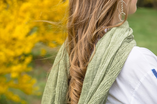 Muchacha rubia con una bufanda elegante del pantano verde entre las flores amarillas brillantes