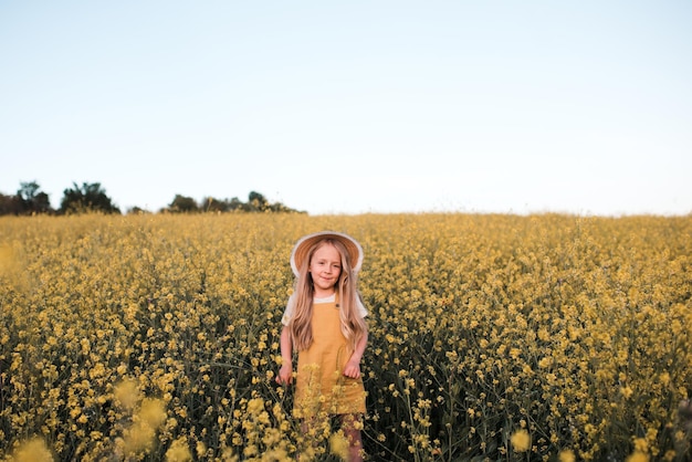 Muchacha rubia divertida del niño que presenta en el prado floreciente de las flores de la violación sobre el fondo de la naturaleza