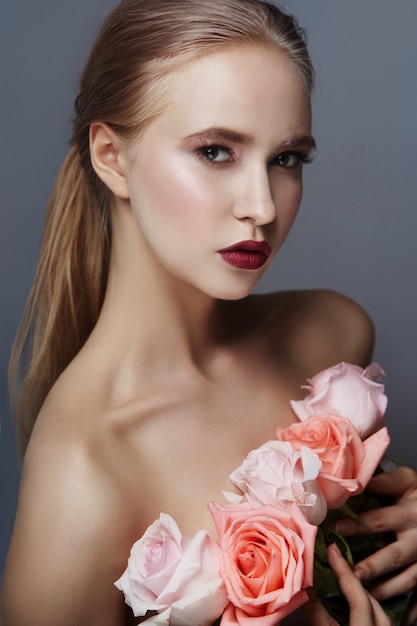 La muchacha rubia que sostenía las flores color de rosa acerca a cara. Belleza