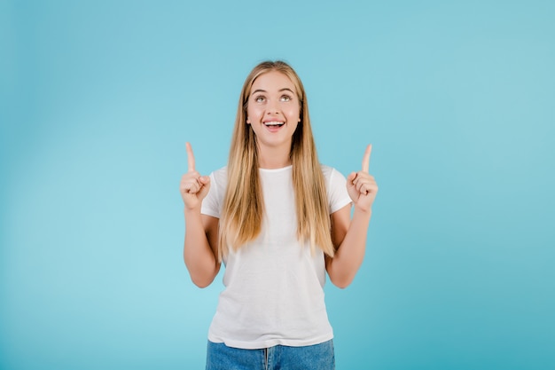 Muchacha rubia sonriente positiva que señala los dedos en el copyspace aislado sobre azul