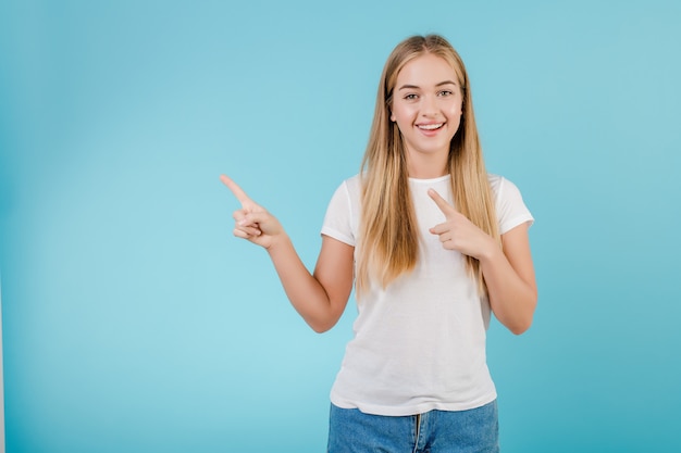 Muchacha rubia sonriente positiva que señala los dedos en el copyspace aislado sobre azul