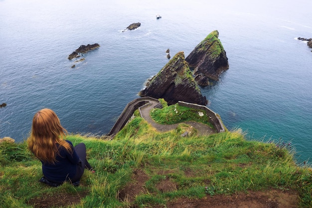 La muchacha se sienta en un acantilado sobre el océano en Irlanda