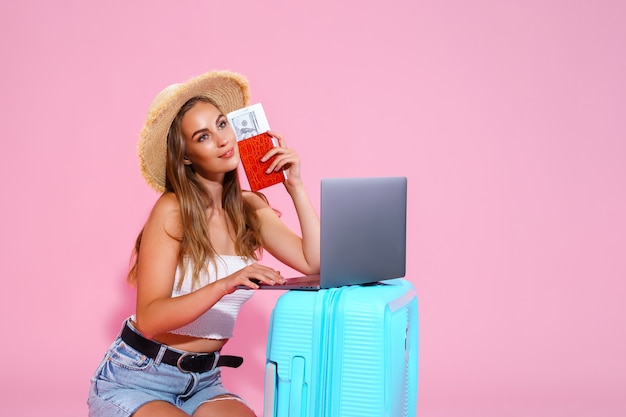 La muchacha sonriente con el dinero de los billetes del ordenador portátil y el pasaporte va a viajar sentado cerca de la maleta en sho ...