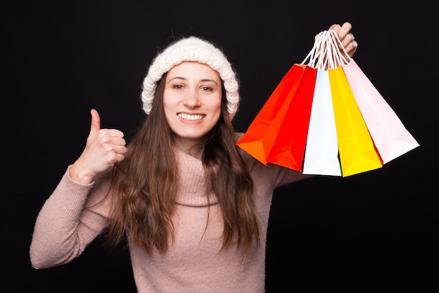 La muchacha sonriente está mostrando el pulgar hacia arriba y sosteniendo algunas bolsas de la compra.