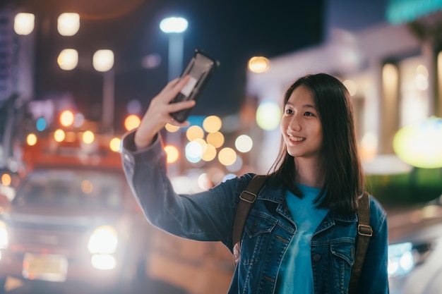 Muchacha sonriente feliz hermosa joven que hace la foto del selfie en calle de la noche