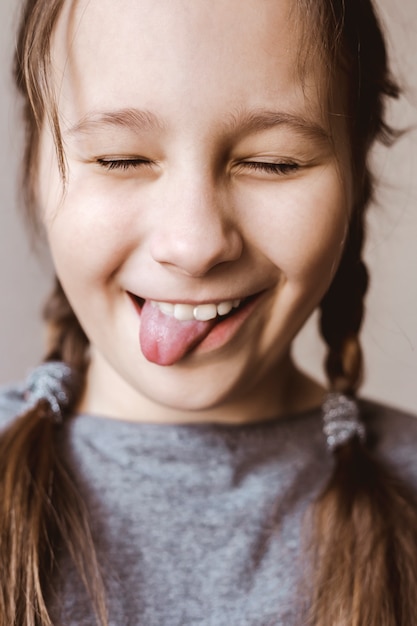 Muchacha sonriente y feliz del niño que muestra la lengua sobre el fondo blanco.