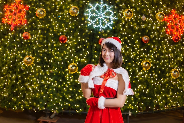 La muchacha sonriente feliz de Papá Noel es linda en traje rojo con el fondo del árbol de navidad