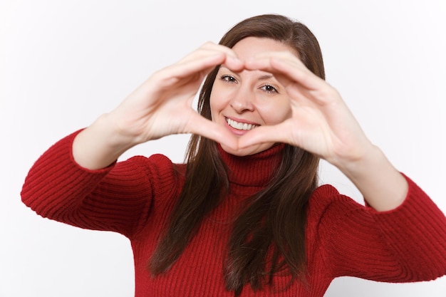 Foto muchacha sonriente de la mujer joven en ropa roja ocasional aislada en el retrato blanco del estudio del fondo. concepto de estilo de vida de emociones de personas. burlarse del espacio de la copia. mostrando forma de corazón con las manos, signo de forma de corazón.