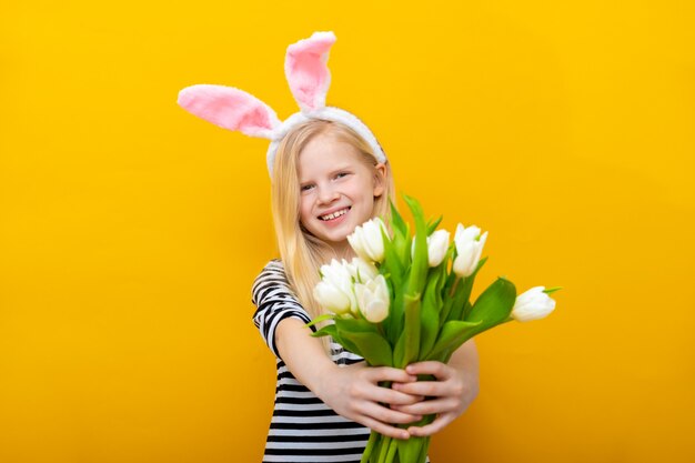 La muchacha sonriente en oídos del conejito del conejo en la cabeza con los tulipanes florece el ramo en fondo amarillo.