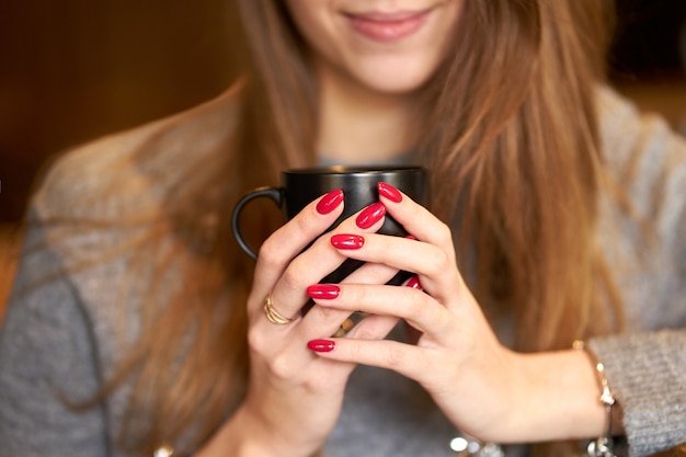 Muchacha sonriente con las uñas rojas que sostienen una taza de café.